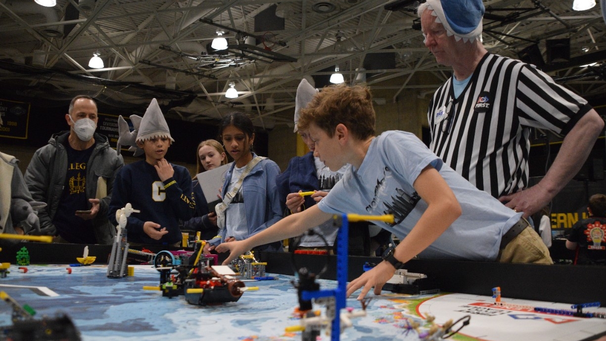 Elementary aged students wearing fun shark hats intently watch their team's LEGO robot perform at the annual Kentucky robotics competition at Northern Kentucky University.