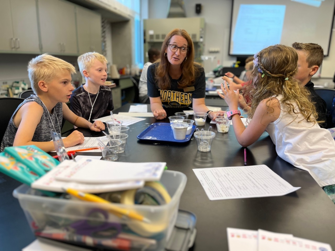 Elementary Engineers Camp Young campers have an engaging discussion with a camp leader while doing an experiment