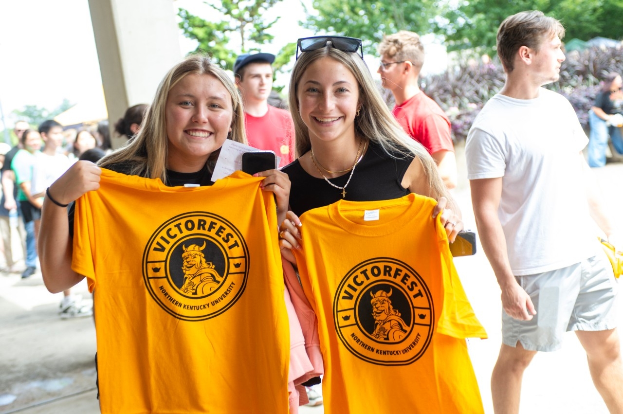 Two female students holding up gold Victorfest t-shirts.